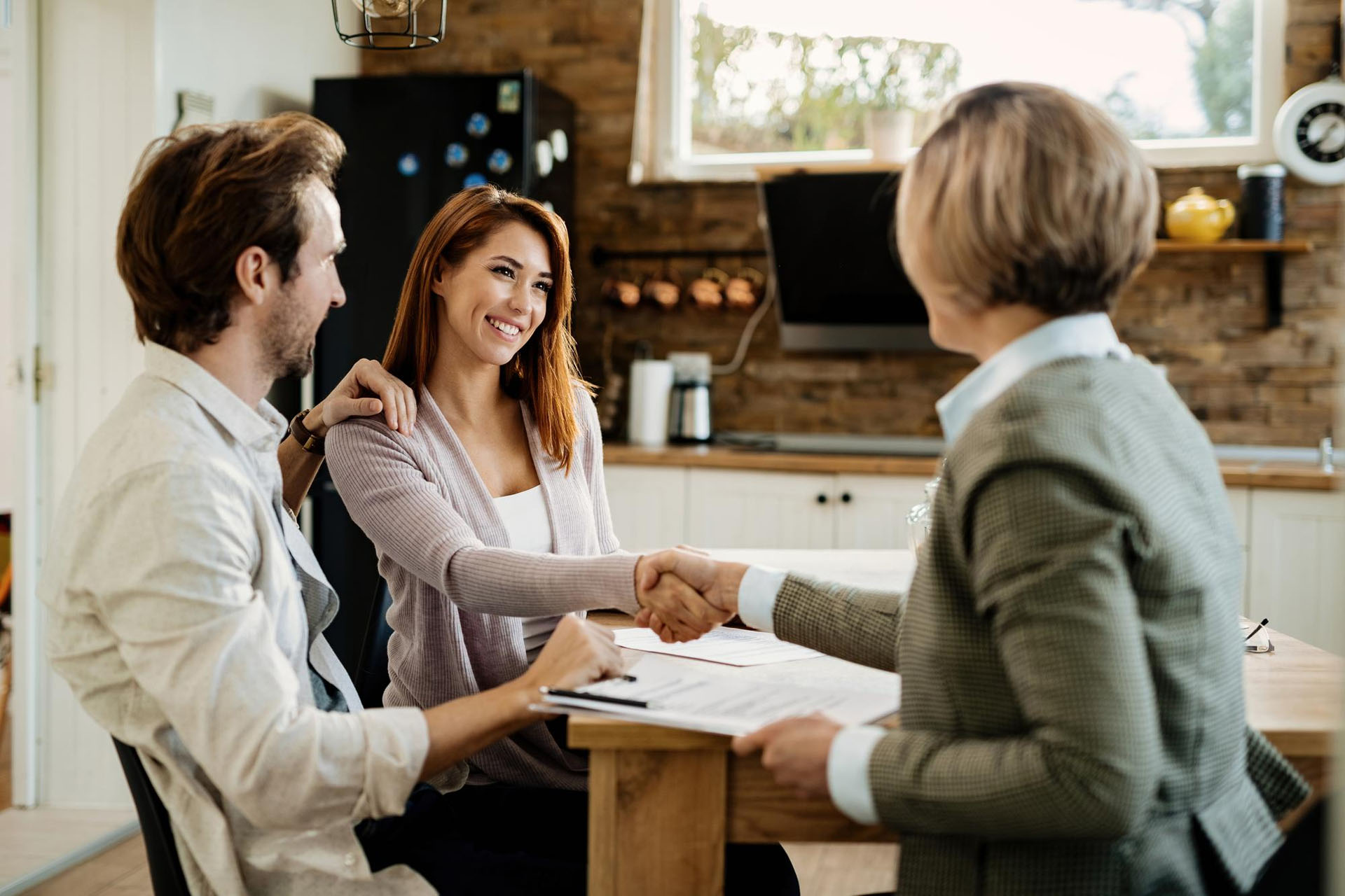happy couple making deal with financial advisor meeting home focus is woman shaking hands with advisor